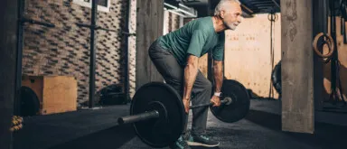 Active elderly man doing a deadlift workout in a gym area of a gym