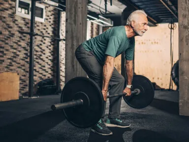 Active elderly man doing a deadlift workout in a gym area of a gym