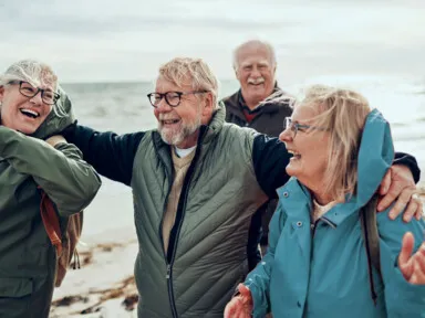 Two couples smiling together while walking on a beach near the ocean