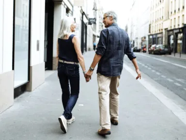 A couple walks down a city street on the sidwalk holding hands