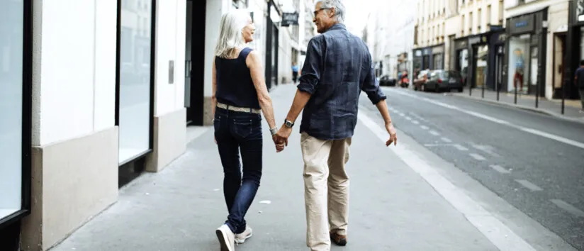 A couple walks down a city street on the sidwalk holding hands