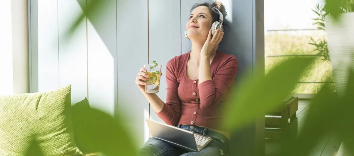 Smiling woman with headphones and laptop sitting outside drinking clean water.