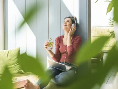 Smiling woman with headphones and laptop sitting outside drinking clean water.