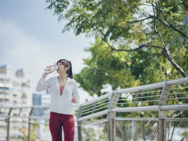 Asian woman drinking from reusable bottle while jogging outdoors hydrated exercise