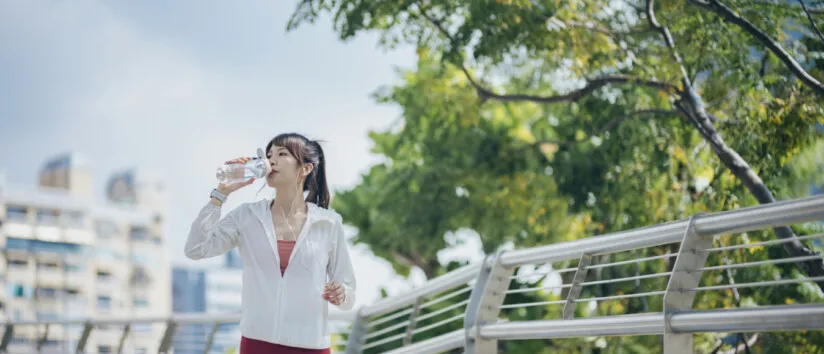 Asian woman drinking from reusable bottle while jogging outdoors hydrated exercise