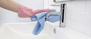 Woman cleaning hard water stain off the faucet with microfiber cloth and gloves