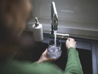 Close up of a senior woman's hand filling a glass of filtered water from the kitchen sink tap. Cost of a water softener