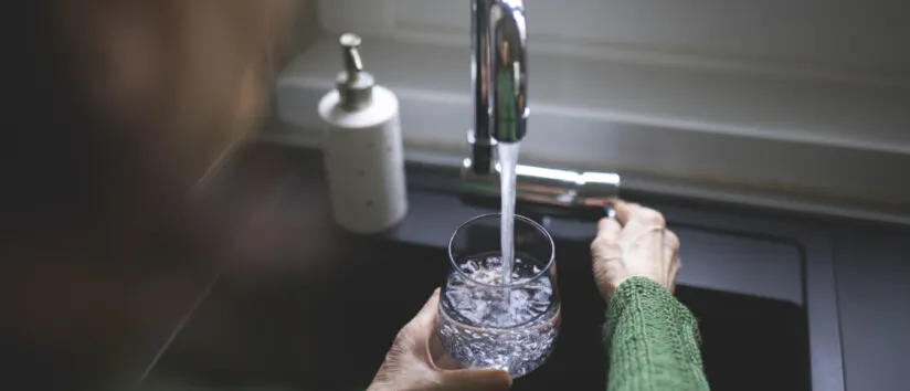 Close up of a senior woman's hand filling a glass of filtered water from the kitchen sink tap. Cost of a water softener