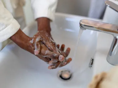 Close-up of a person lathering hands with soap and water over a bathroom sink, promoting soft water