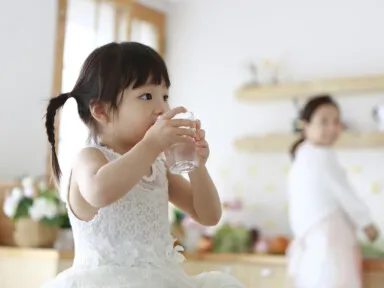 Little girl drinking glass of water in kitchen. tap water is safe to drink