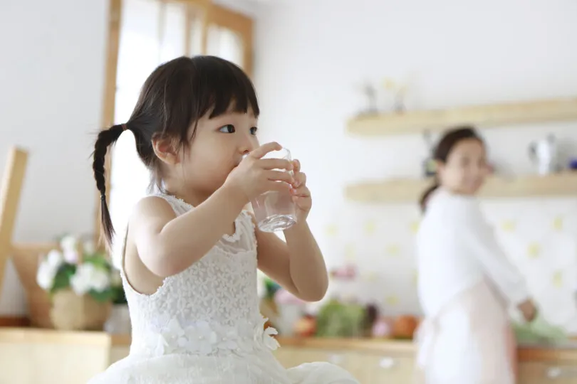 Little girl drinking glass of water in kitchen. tap water is safe to drink