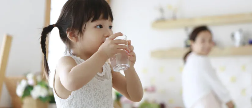 Little girl drinking glass of water in kitchen. tap water is safe to drink