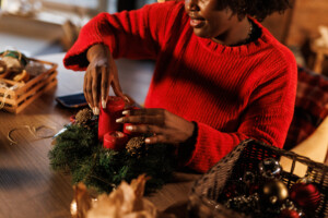 Cut out shot of young woman adding red candles inside the Christmas wreath that she is decorating with pinecones. Decor to conserve water at home.