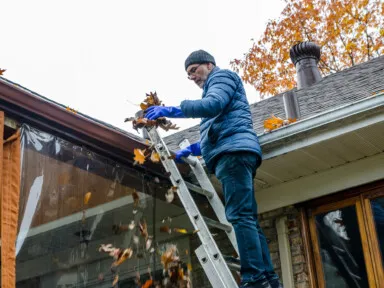 Man on ladder removing leaves from gutter practicing proactive home maintenance